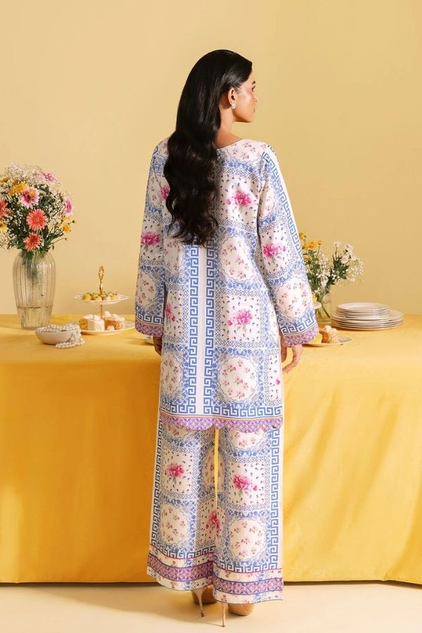 Woman in a patterned outfit standing in front of a yellow table with floral arrangements.