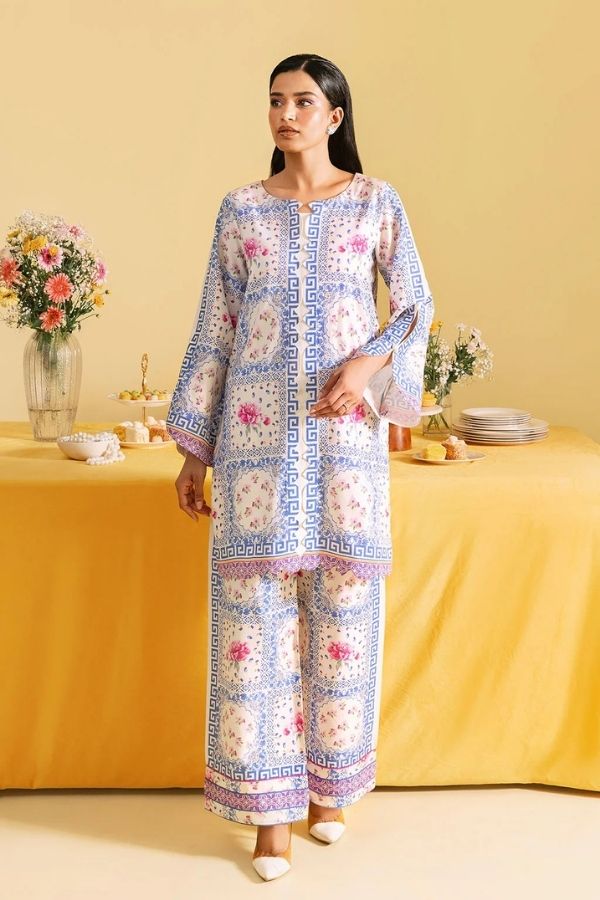 Woman in a floral outfit standing in front of a yellow tablecloth with decorative items.