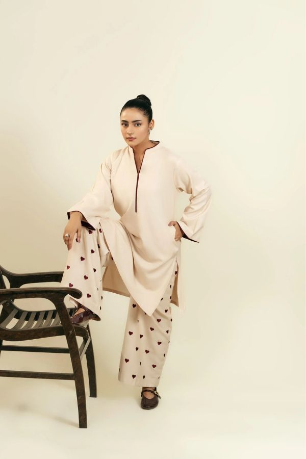 Woman wearing a light pink outfit with heart patterns, sitting on a chair against a plain background.