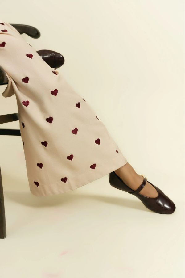 Person wearing beige pants with red heart patterns and black shoes on a light background