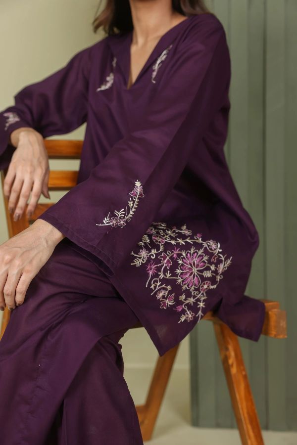 Person wearing a purple embroidered outfit sitting on a wooden chair.