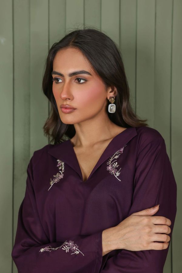Woman wearing a purple embroidered blouse against a green background