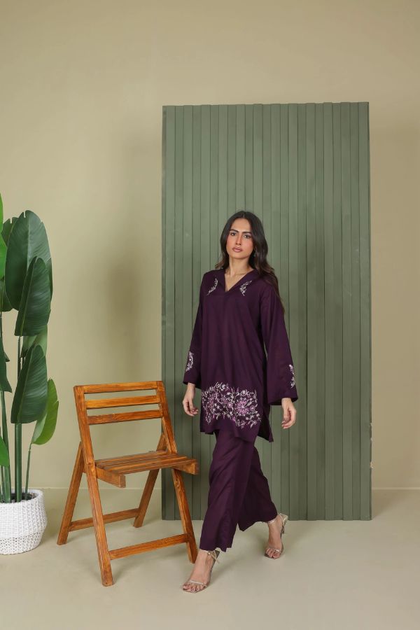 Woman in a purple outfit standing next to a wooden chair and green panel on a beige wall.