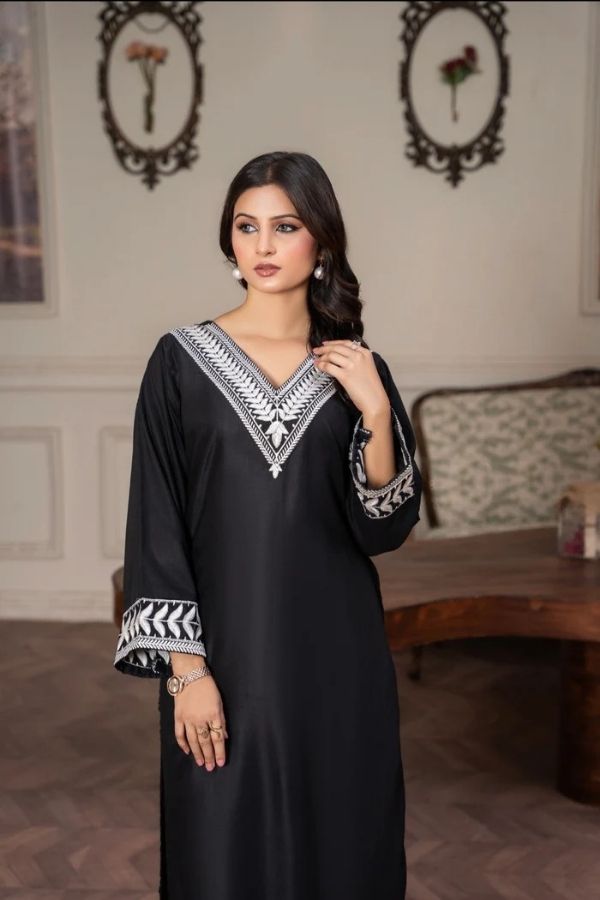Woman wearing a black dress with white embroidery in an indoor setting