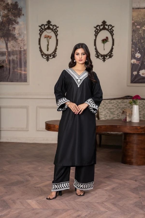 Woman in a black traditional outfit with white patterns standing in an elegant room.