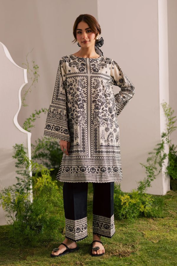 Woman wearing a black and white patterned outfit standing outdoors with greenery around.