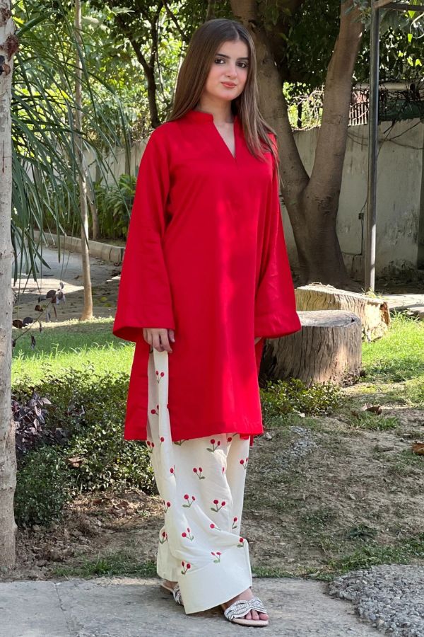 Woman wearing a red top and white pants with red patterns outdoors.