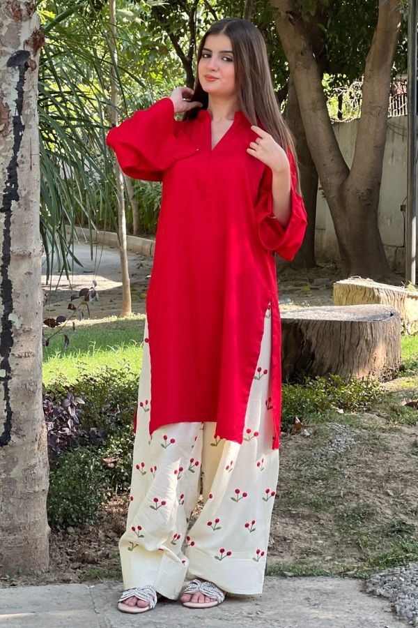 Woman wearing a red top and white pants with red patterns outdoors.