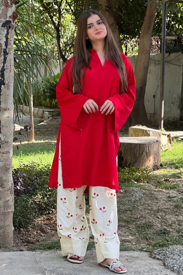 Woman wearing a red top and white pants with floral patterns outdoors.