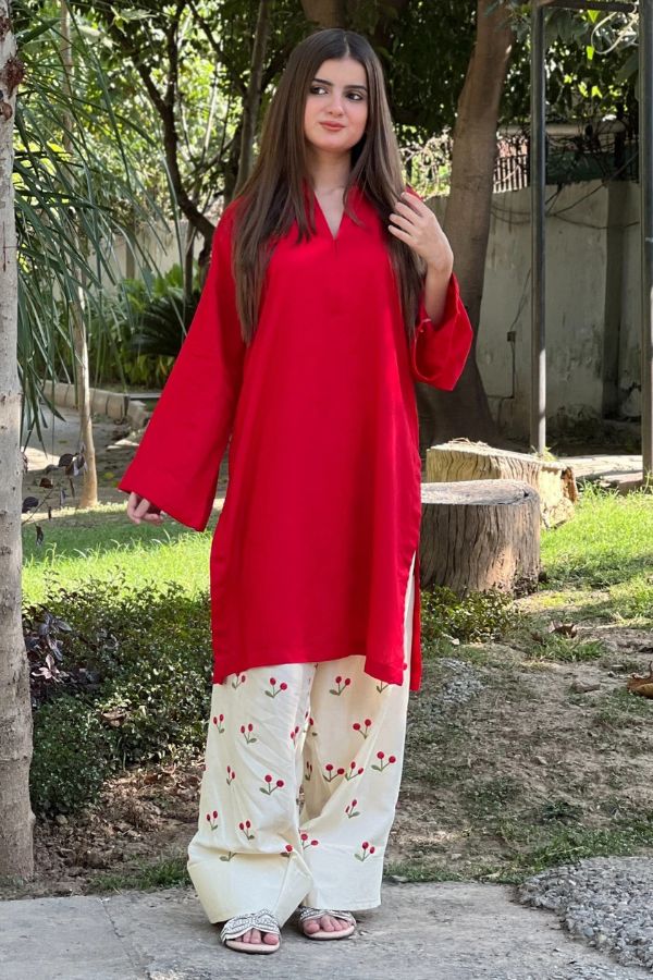 Woman wearing a red top and white pants with red patterns outdoors.