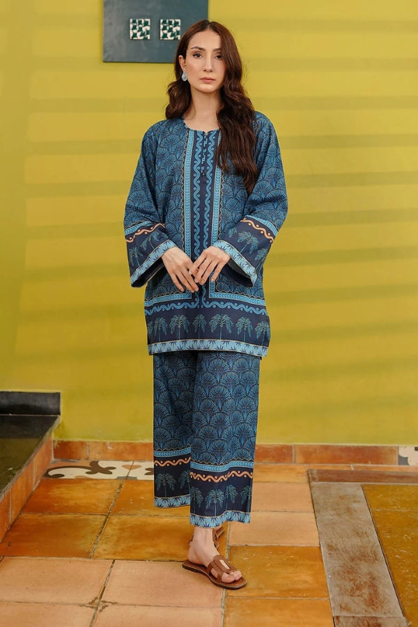 Woman wearing a blue patterned outfit standing against a yellow wall.