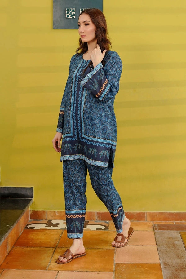 Woman wearing a blue embroidered outfit standing against a yellow wall.