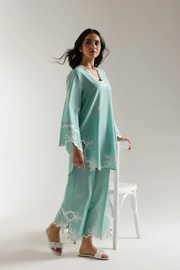 Woman wearing a light blue outfit with white lace details on a plain background