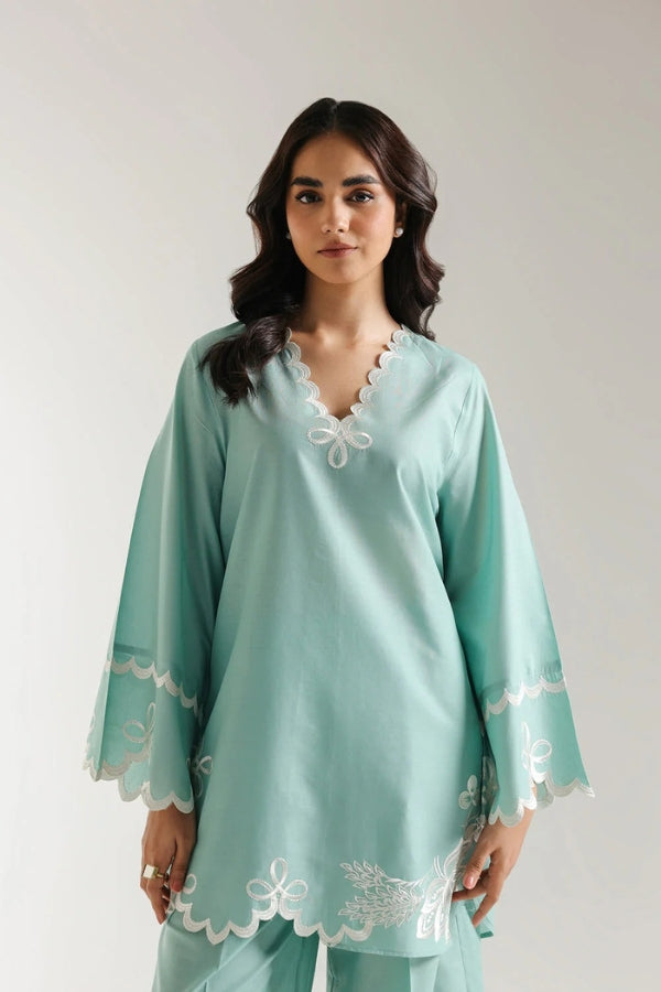 Woman wearing a light blue outfit with white lace details on a plain background