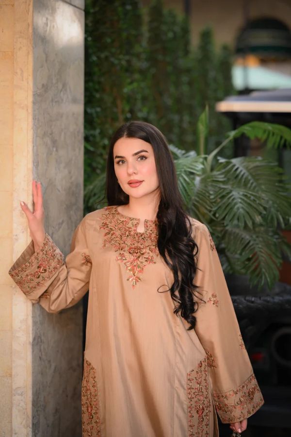 Woman wearing a beige embroidered outfit standing outdoors with greenery in the background