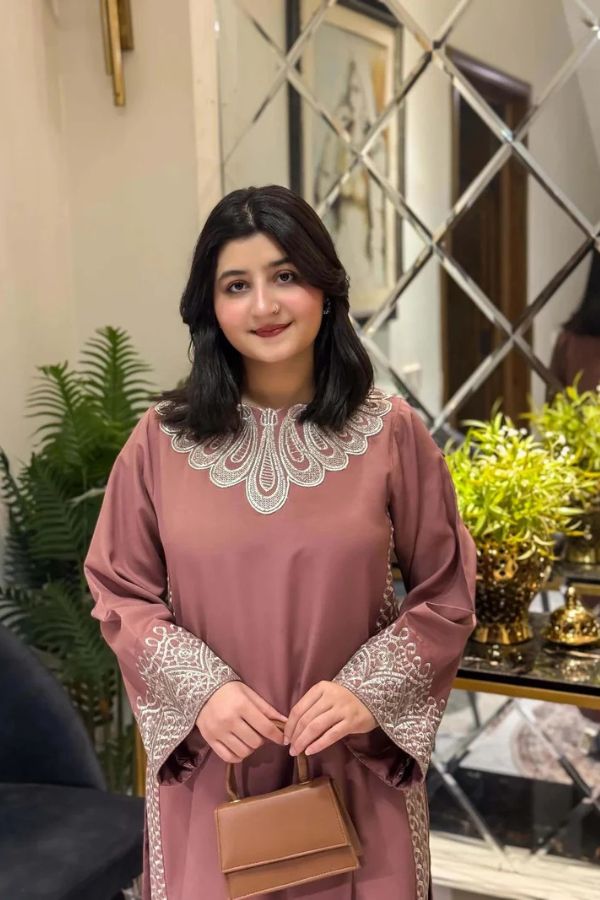 Woman in a pink traditional outfit with lace details standing indoors.