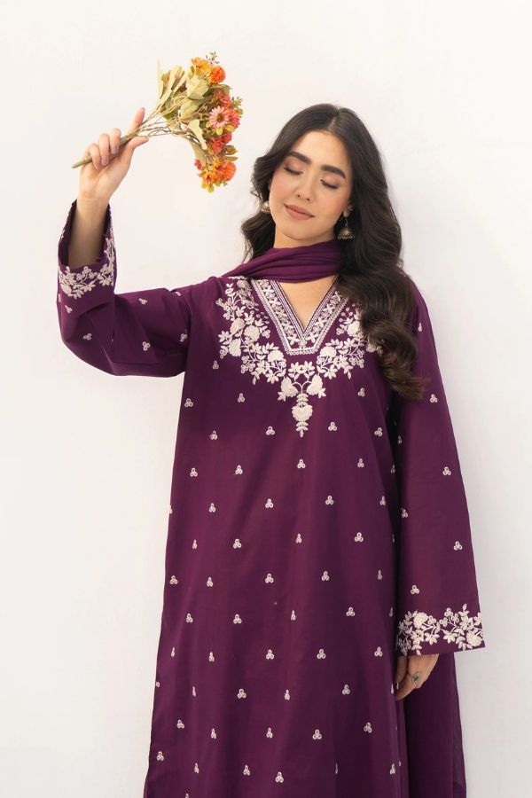 Woman wearing a purple embroidered dress holding a bouquet of flowers against a white background