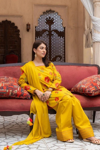 Premium mustard lawn suit by Ragini featuring delicate floral embroidery, embroidered lawn shirt, dyed trousers, and flowing Bamber chiffon dupatta – perfect summer outfit for women in Pakistan, ideal for festive and semi-formal wear.