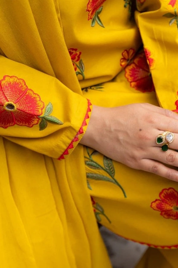 Premium mustard lawn suit by Ragini featuring delicate floral embroidery, embroidered lawn shirt, dyed trousers, and flowing Bamber chiffon dupatta – perfect summer outfit for women in Pakistan, ideal for festive and semi-formal wear.