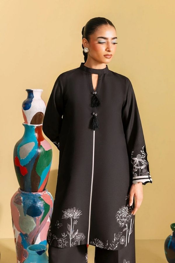 Woman wearing a black dress with white embroidery standing next to colorful vases on a beige background