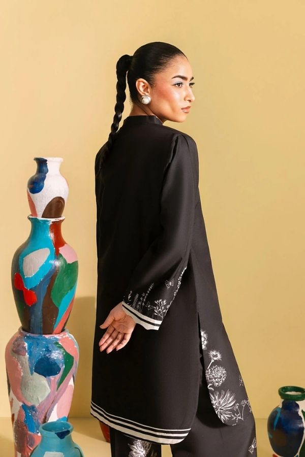 Woman in a black outfit with white patterns standing next to colorful vases against a beige background