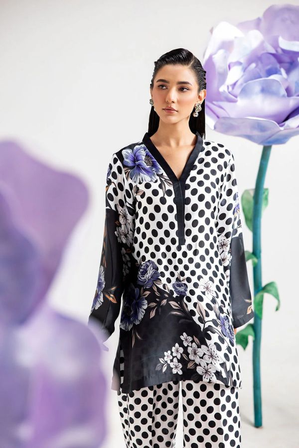 Woman wearing a polka dot outfit with floral patterns, standing against a white background with large purple flowers.