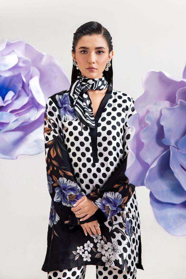 Woman wearing a polka dot outfit with a floral scarf, surrounded by purple flowers.