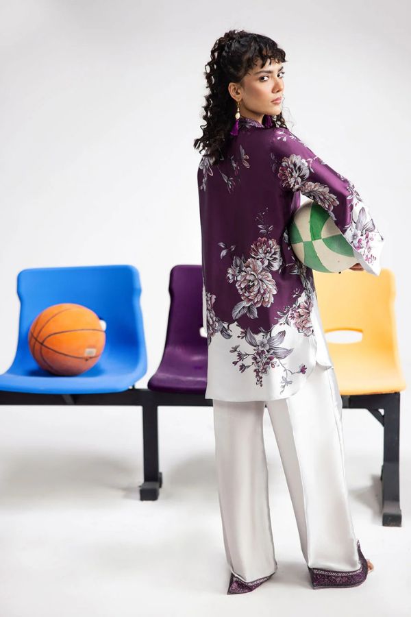 Woman in a floral purple top and white pants holding a sports ball, with colorful chairs in the background.