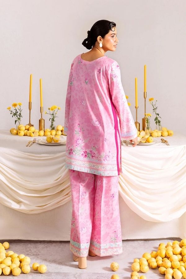 Woman in a pink traditional outfit standing in front of a decorated table with candles and flowers.