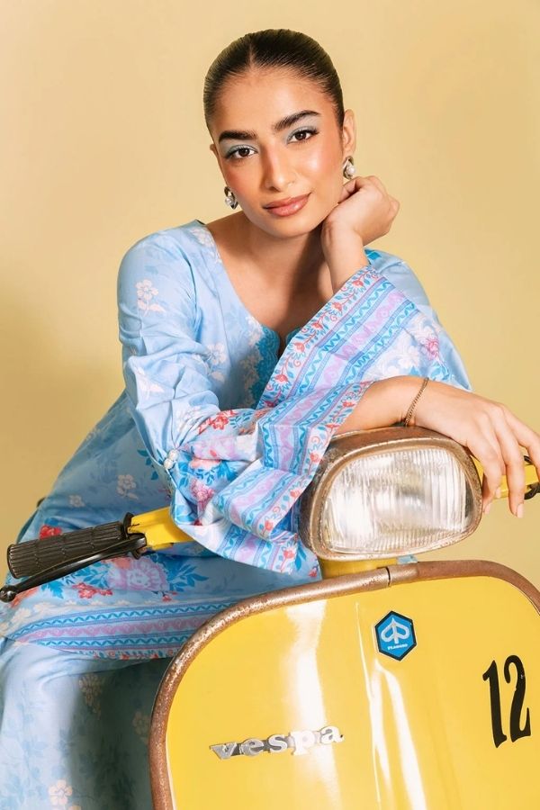 Woman in a blue traditional outfit sitting on a yellow scooter with a beige background