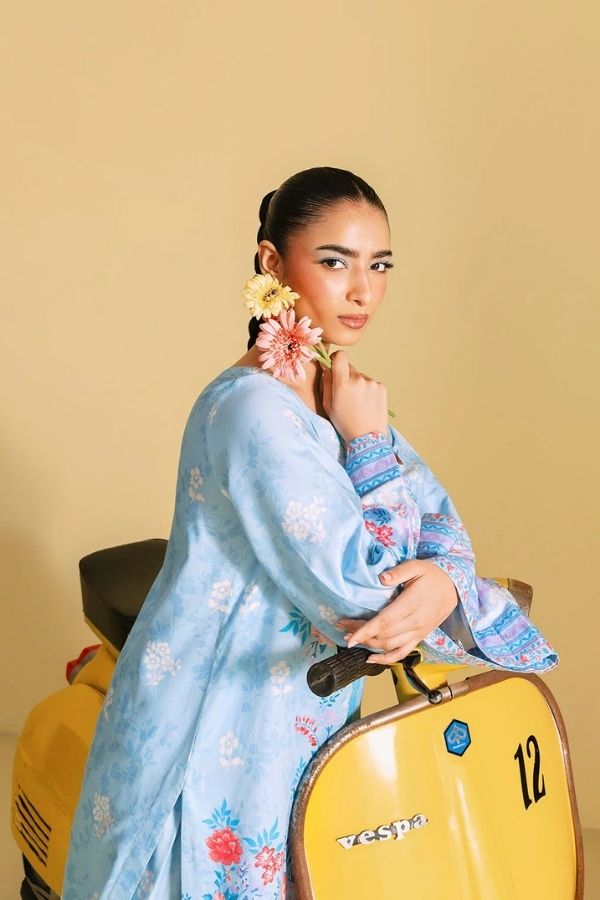Woman in a light blue floral dress sitting on a yellow Vespa against a beige background