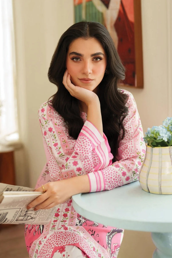 Woman in a pink and white patterned outfit sitting at a table with a newspaper, in a room with a vase of flowers and a painting on the wall.