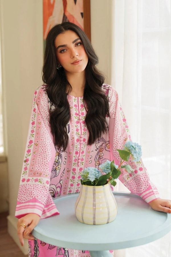 Woman in a pink floral dress standing next to a table with a vase of flowers.