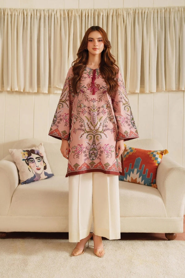 Woman wearing a pink embroidered kurta with white pants in a living room setting.