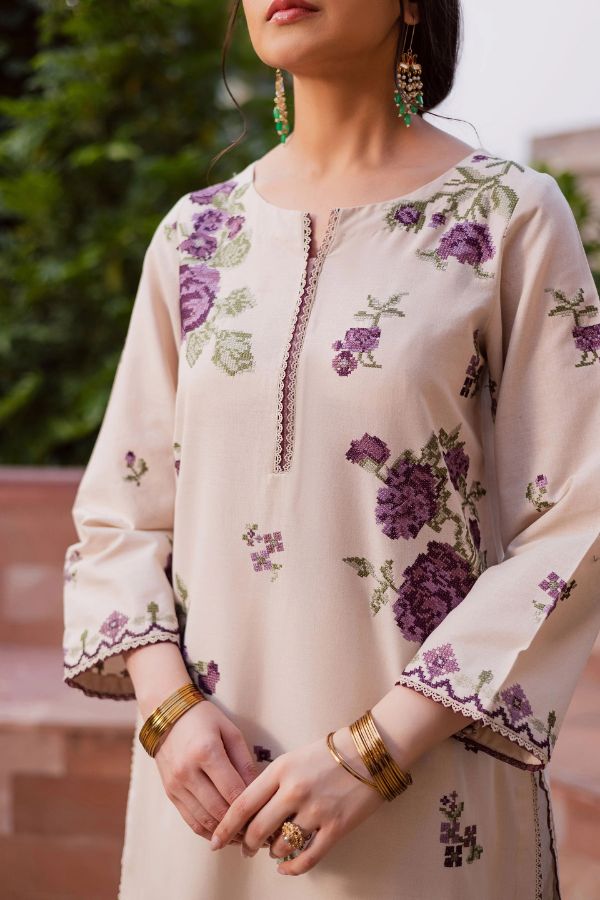 Beige kurta with floral embroidery worn by a person, with a blurred green background