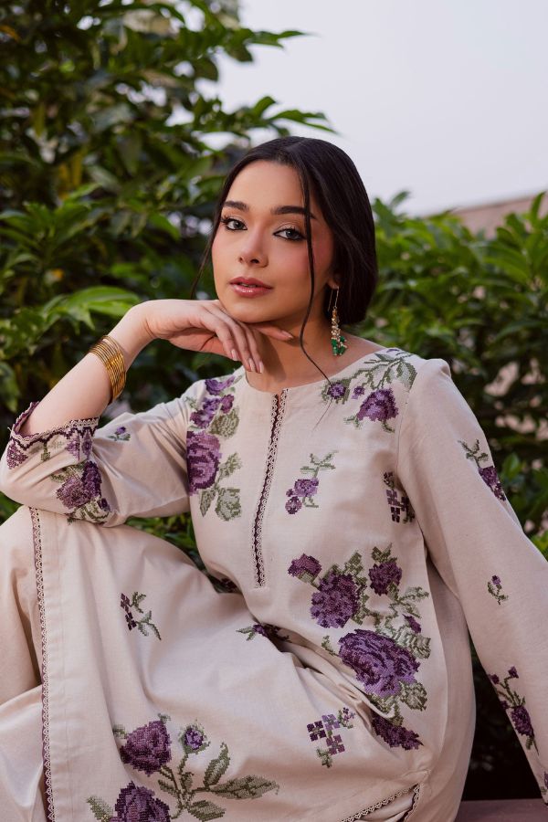 Woman wearing a beige outfit with purple floral embroidery sitting outdoors.