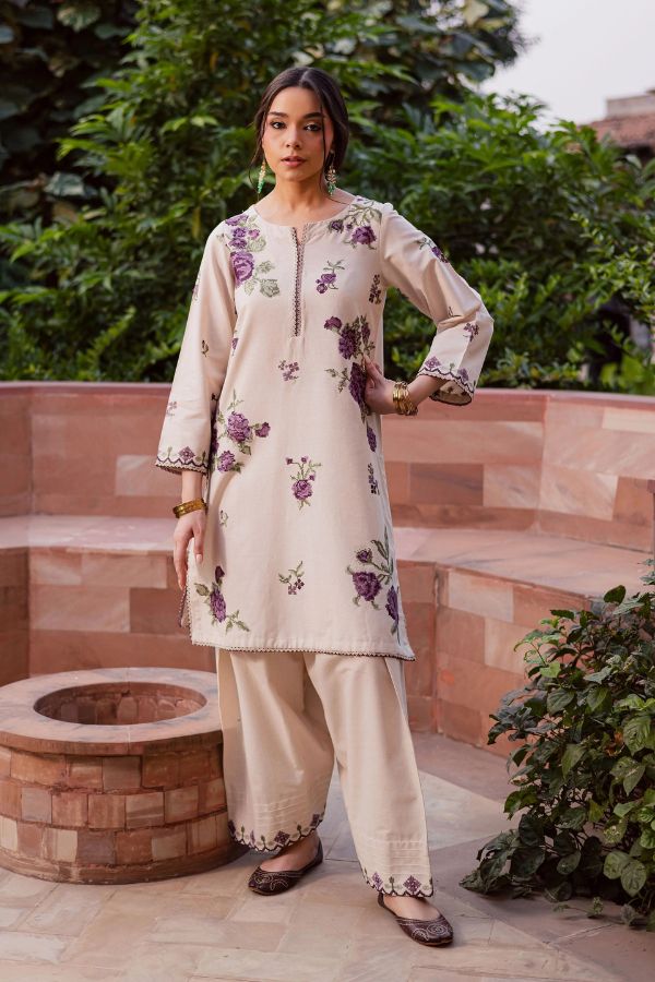 Woman wearing a cream-colored traditional outfit with floral patterns in an outdoor setting.