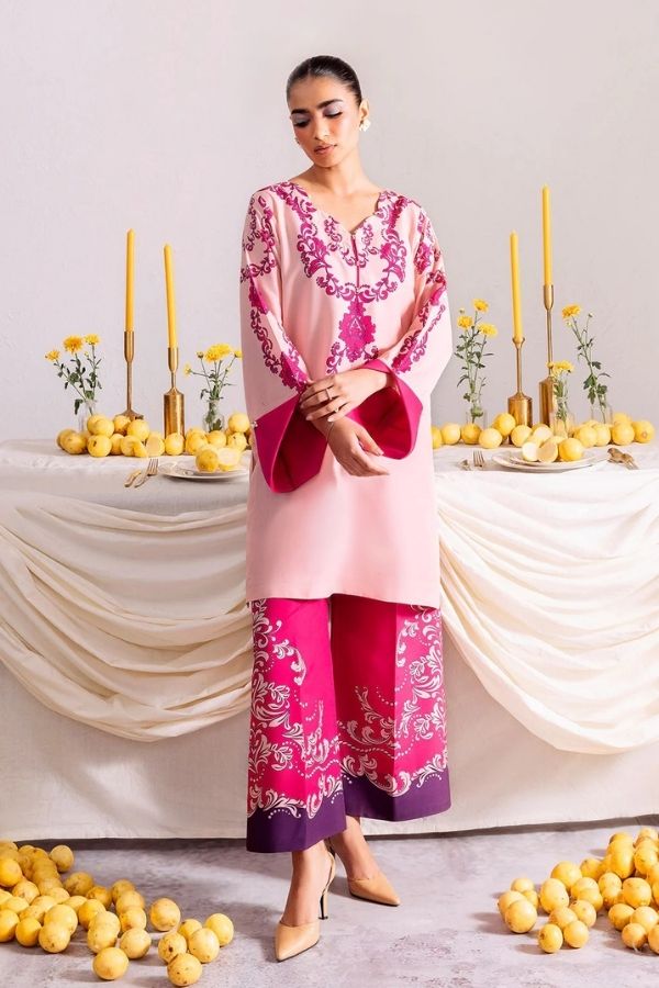 Woman in a pink and purple traditional outfit standing in front of a decorated table with candles and flowers.