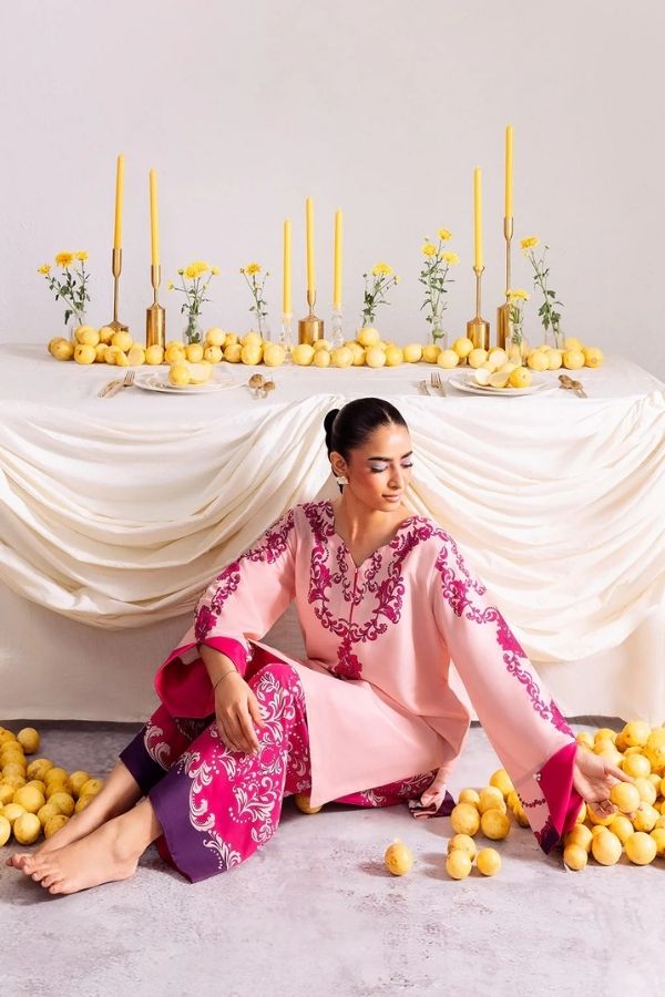 Woman in a pink and purple traditional outfit sitting on the floor with lemons and candles in the background.