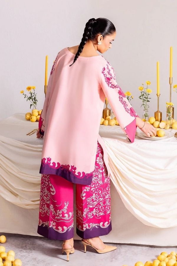 Woman in a pink and purple traditional outfit arranging flowers on a table.