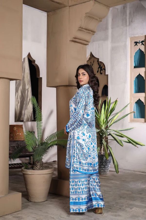 Woman in a blue patterned outfit standing in a room with plants and architectural elements.