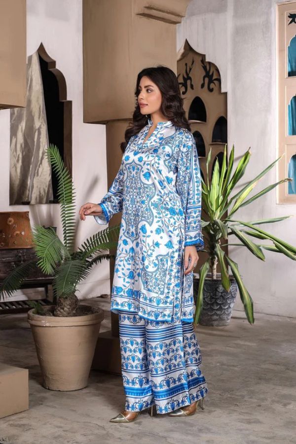 Woman in a blue and white patterned outfit standing in a room with plants and decorative items.