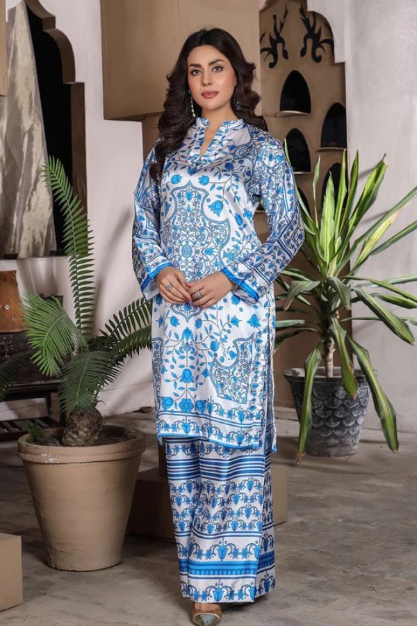 Woman wearing a blue and white patterned traditional outfit standing in a room with plants.