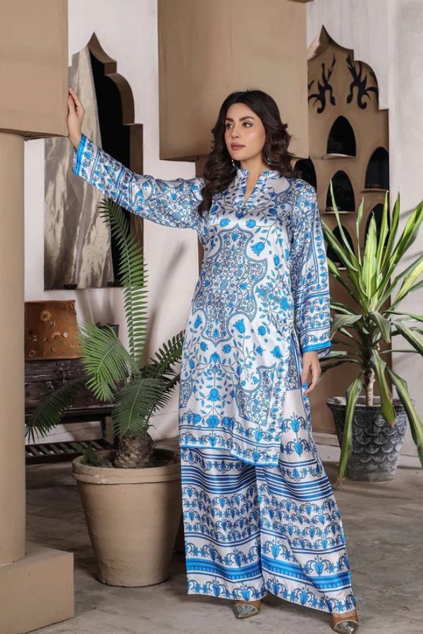 Woman in a blue and white patterned dress standing in a room with plants and architectural elements.