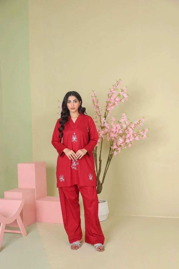 Woman in a red outfit standing in a room with pink chairs and a plant.