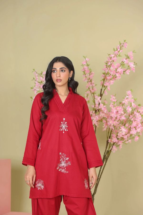 Woman wearing a red outfit with floral embroidery against a beige background with pink flowers.