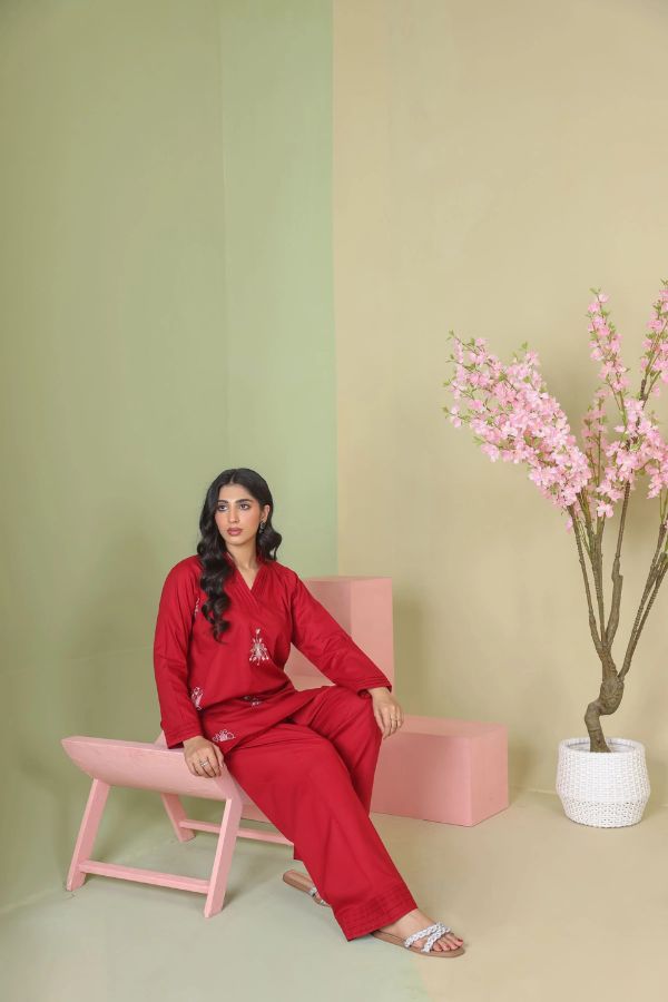 Woman in red outfit sitting on a pink chair against a green and beige wall with a plant.