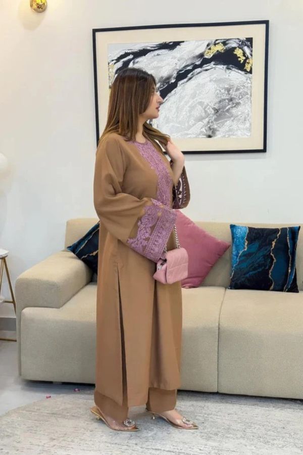 Woman in a beige outfit standing in a living room with a couch and framed artwork.