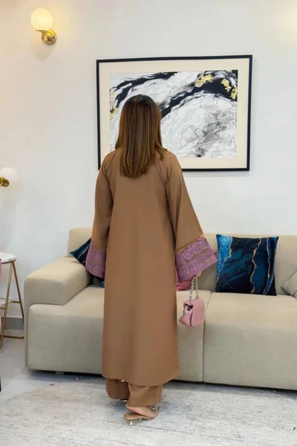 Woman in a beige outfit standing in a living room with a beige sofa and framed artwork on the wall.