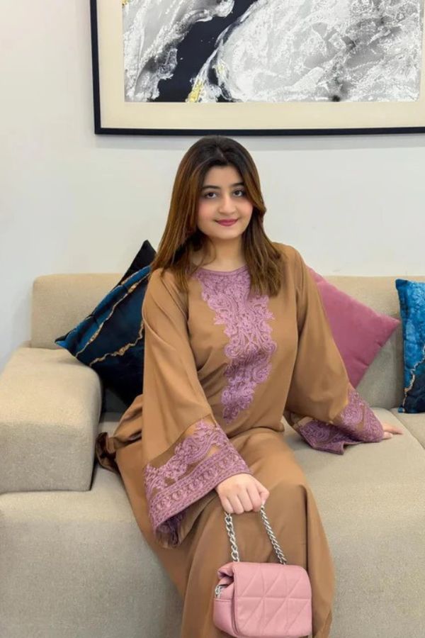 Woman in a brown and purple outfit sitting on a couch with a pink handbag.